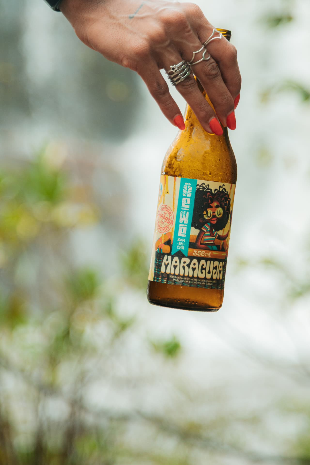Mão segurando EWE Kombucha Maracujá em meio à natureza