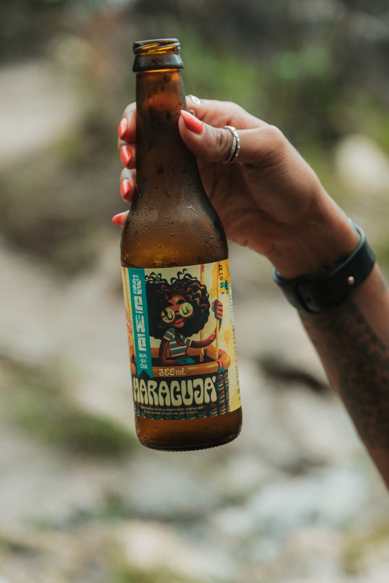 Mão segurando uma garrafa de EWE Kombucha Maracujá na natureza
